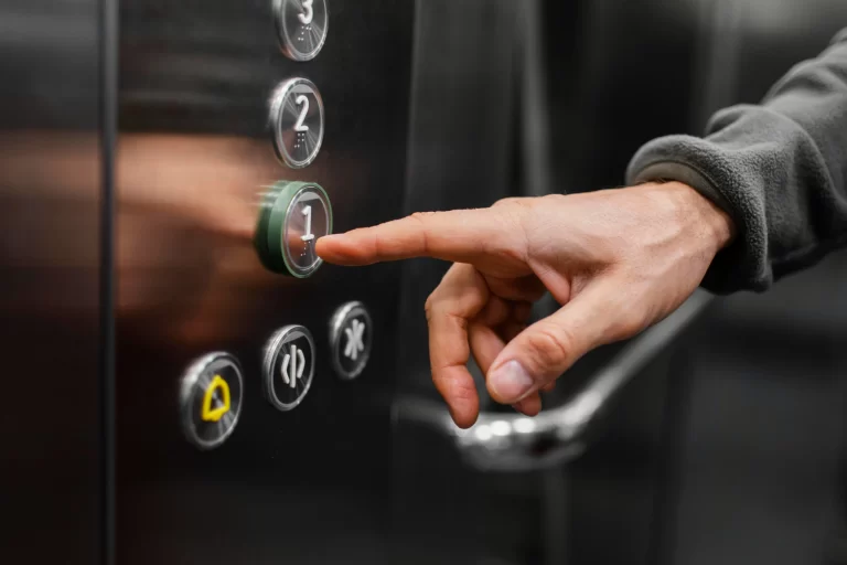 Close-up da mão de um homem pressionando o botão de primeiro andar de um elevador, para ilustrar a importância da manutenção de elevadores para garantir a segurança e funcionalidade do sistema.