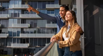 Um casal olha para a vista na varanda de um condomínio residencial.