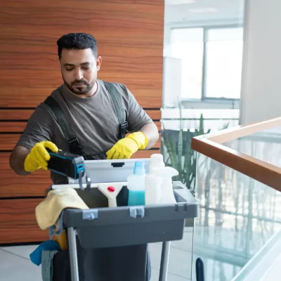 Um profissional de limpeza utilizando equipamentos e produtos em um carrinho de limpeza, demonstrando a importância da terceirização de serviços em condomínios.